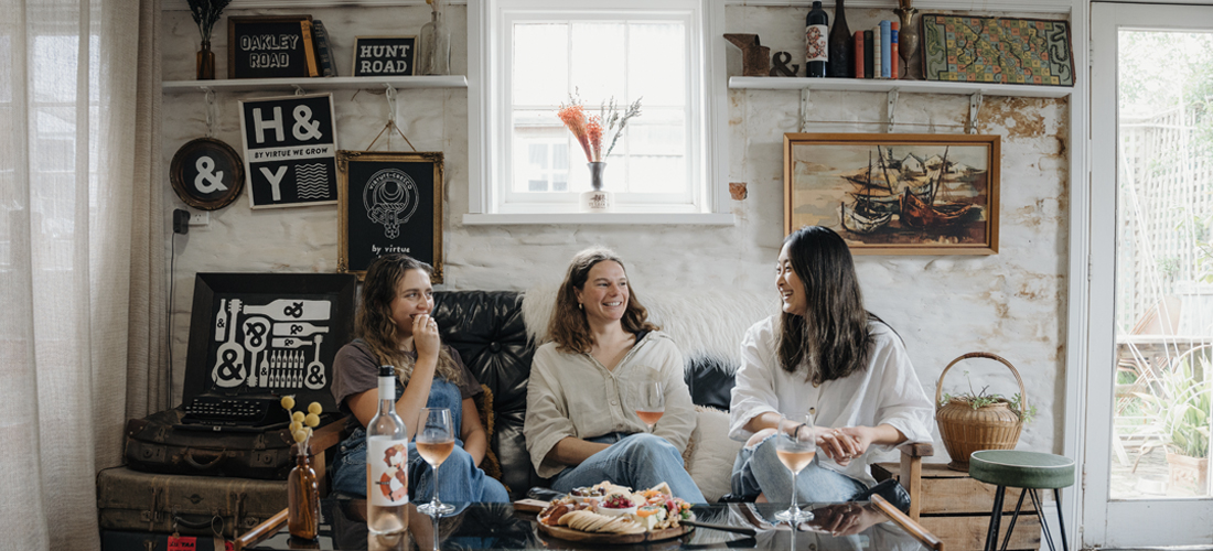 Three women on a  sofa enjoying wine and food